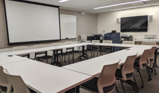 Allen library large seminar room, with podium, projector screen, TV display, keyboard, and tables